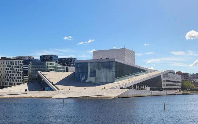 Panorámica del edificio de la Ópera sobre las aguas del fiordo, donde se ven las pequeñas figuras humanas a modo de oscuros pingüinos.