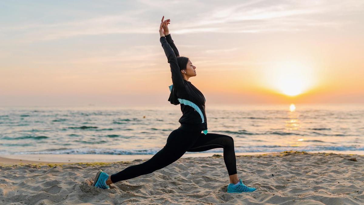 Una mujer hace deporte al amanecer en una playa.