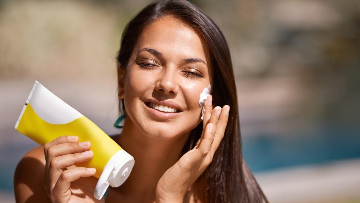Mujer en la piscina se aplica protector solar en la cara.