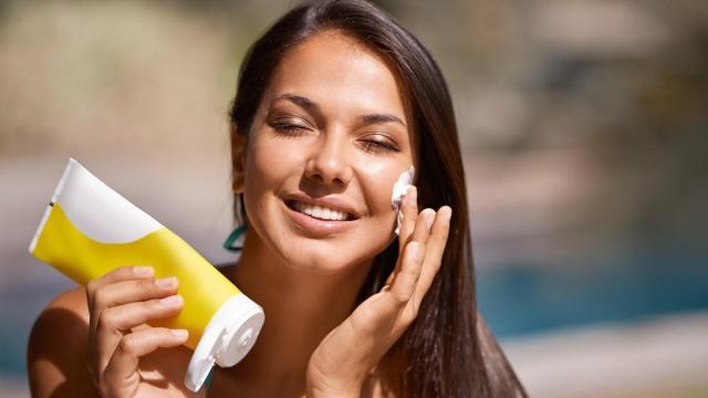 Mujer en la piscina se aplica protector solar en la cara.