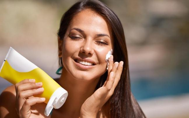 Mujer en la piscina se aplica protector solar en la cara.