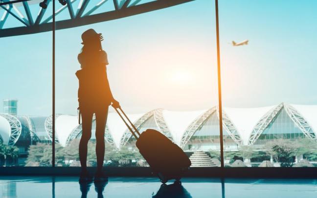 Una mujer observa a través de una cristalera el despegue de un avión. Una mujer observa a través de una cristalera el despegue de un avión.