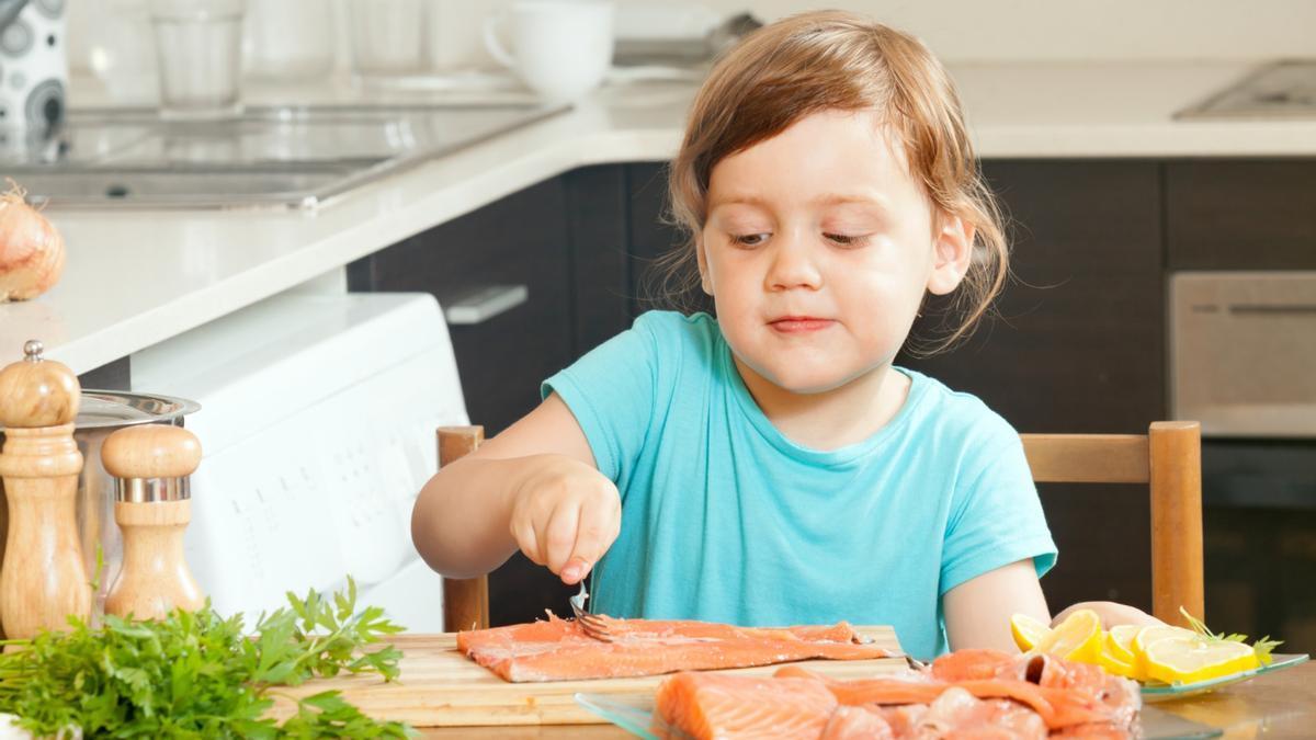 Una niña prepara una tajada de salmón para que pueda ser cocinada