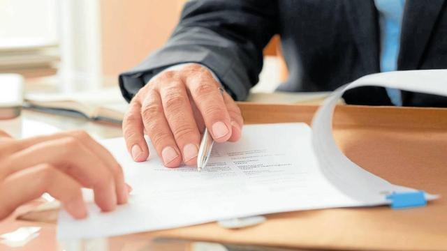 Primer plano de una mesa de despacho donde dos personas revisan un documento.
