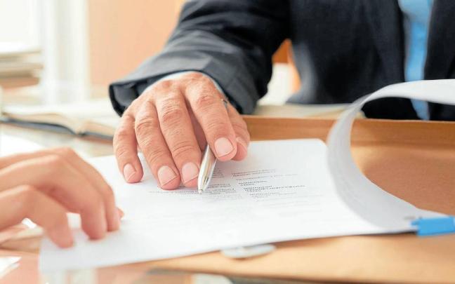 Primer plano de una mesa de despacho donde dos personas revisan un documento.