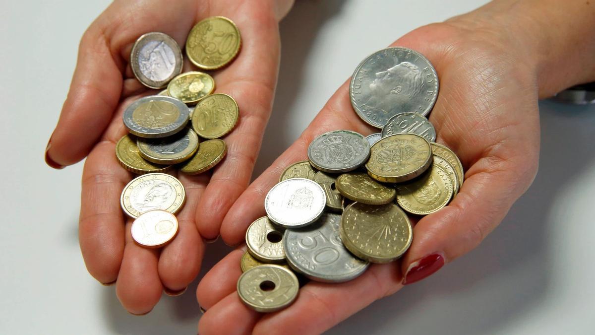 Dos manos con varias monedas de euros y de pesetas