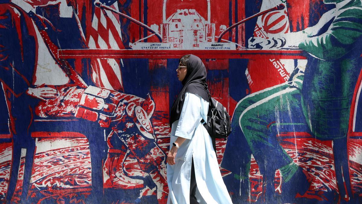 Una iraní pasa junto a un mural en el que se representa una mesa de negociaciones entre Irán y EE.UU., en Teherán.
