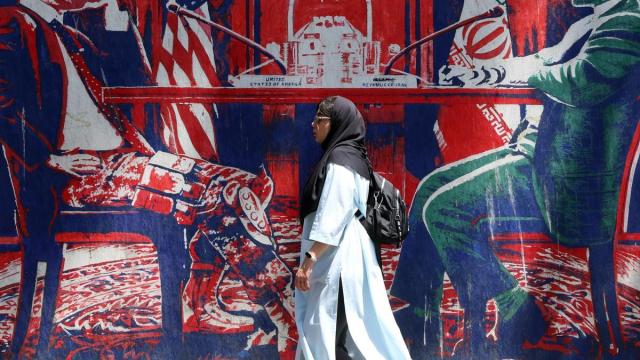 Una iraní pasa junto a un mural en el que se representa una mesa de negociaciones entre Irán y EE.UU., en Teherán.