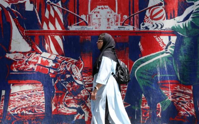 Una iraní pasa junto a un mural en el que se representa una mesa de negociaciones entre Irán y EE.UU., en Teherán.