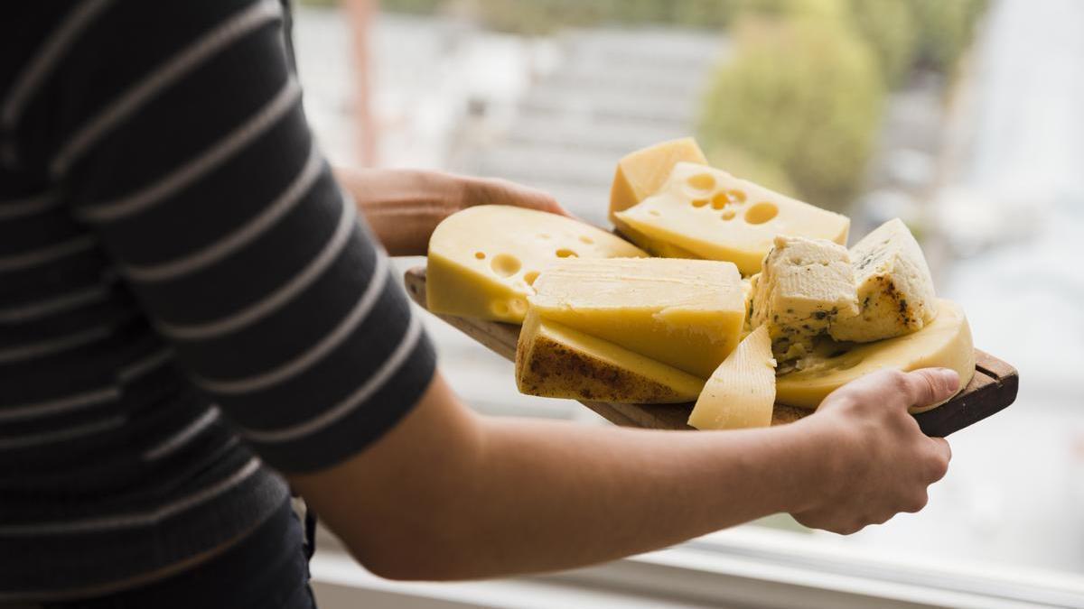 Manos de una persona con una tabla de quesos variados