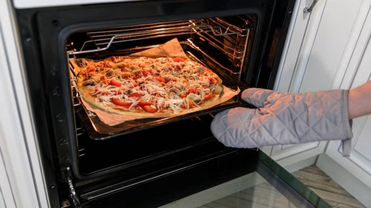 Mano de una chica sacando una pizza casera del horno con ayuda de una manopla para no quemarse.