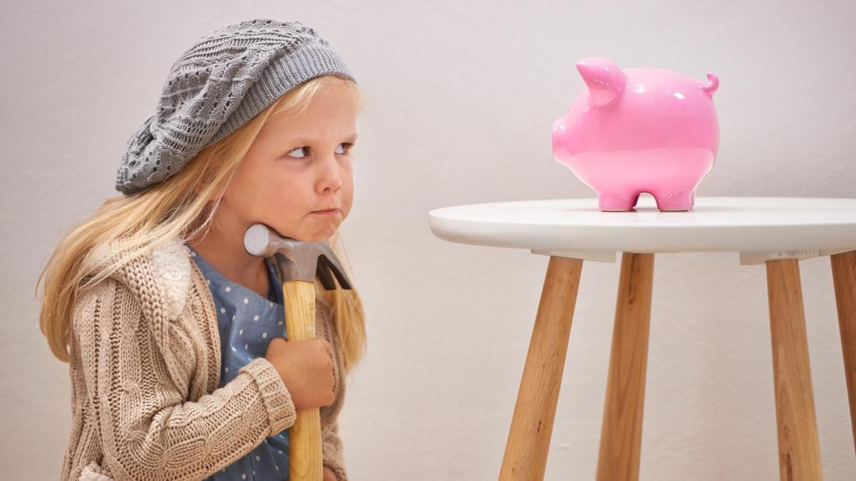 Una niña duda si romper su hucha de cerdito con un martillo.