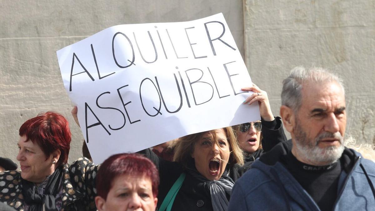 Una mujer, en el centro de la imagen, portando un cartel en el que puede leerse 'alquiler asequible', durante una manifestación.