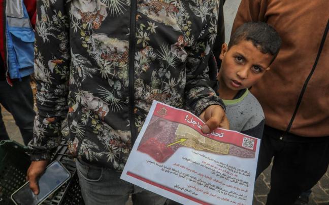 Varios gazatíes leen un cartel donde se insta a evacuar la ciudad de Rafáh.