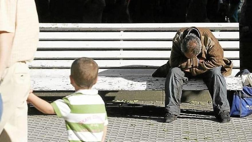 Un niño observa a un mendigo sentado en un banco de una capital vasca