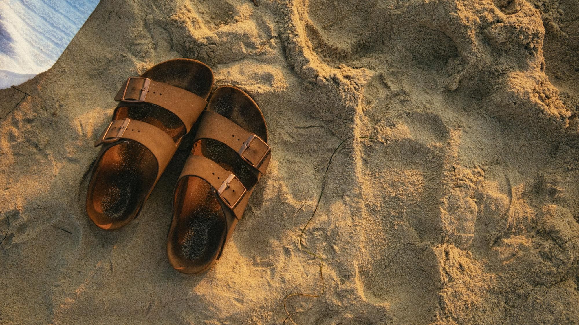 Sandalias sobre la arena con la huella del pie marcada.