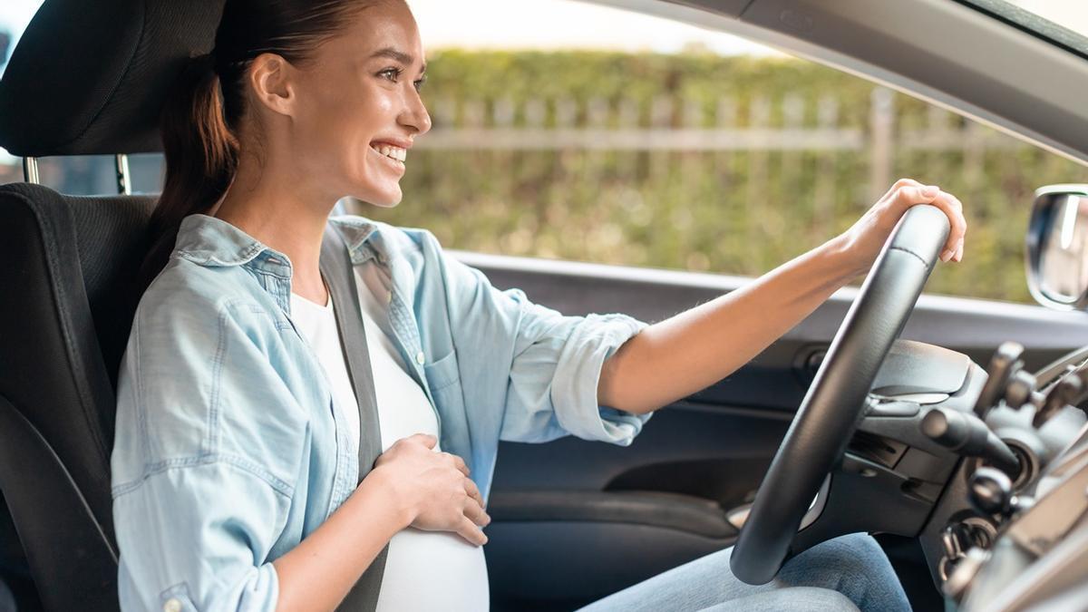 Una mujer embarazada que debería conducir con las dos manos en el volante.