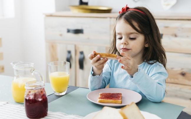 Niña desayuna una tostada con mermelada de fresa y zumo de naranja antes de ir al colegio.
