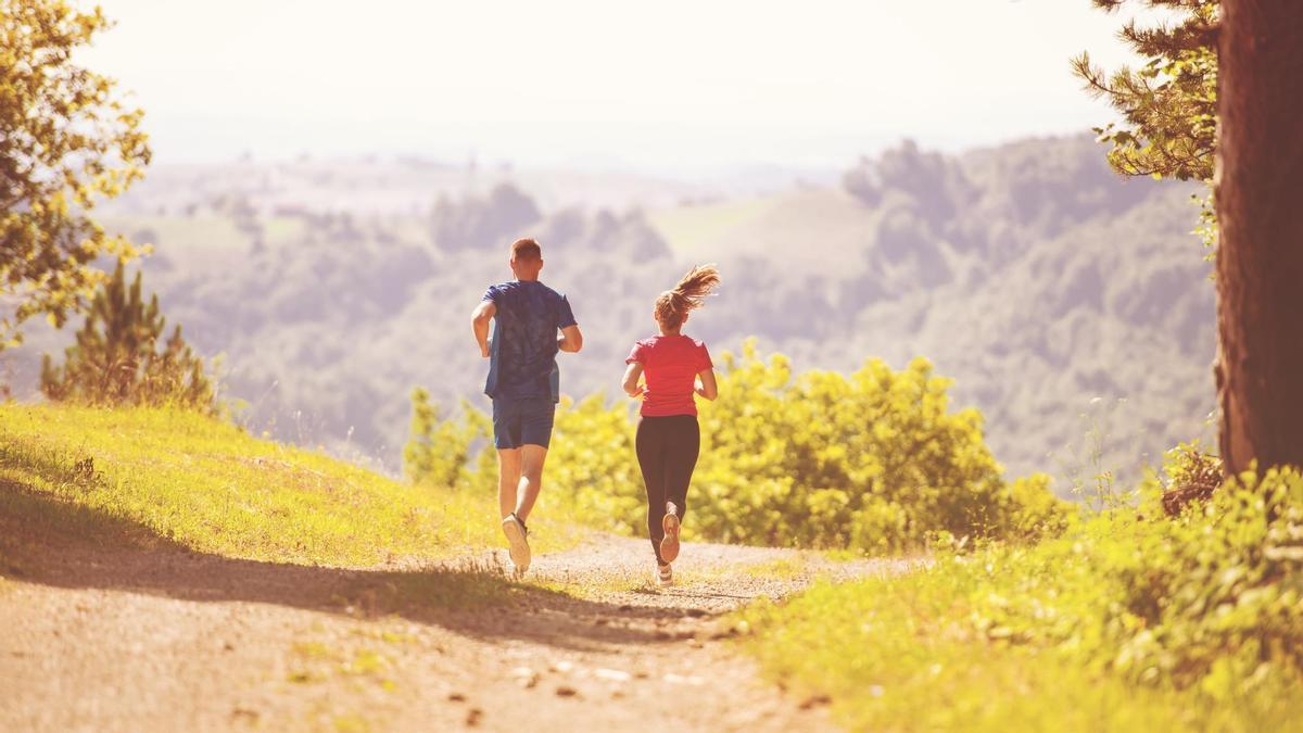 Una pareja corre por el monte en un día soleado.