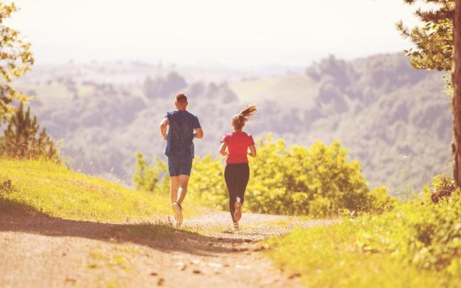 Una pareja corre por el monte en un día soleado.