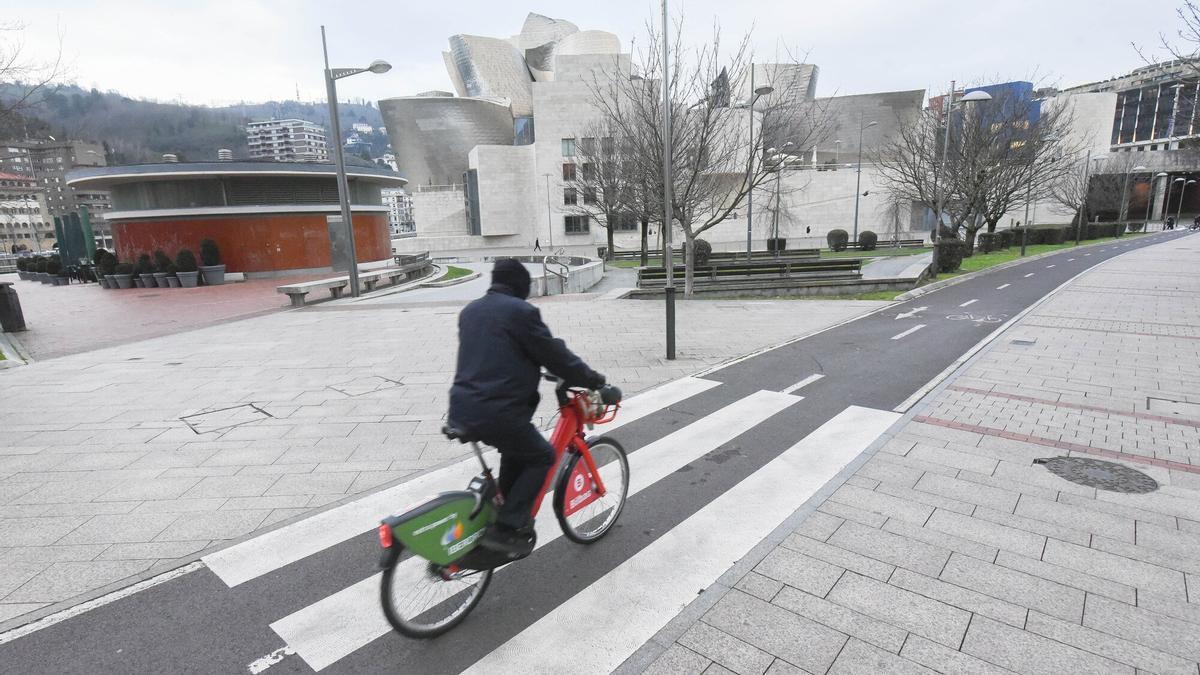 Un hombre pasea en bicicleta con el Guggenheim de fondo.