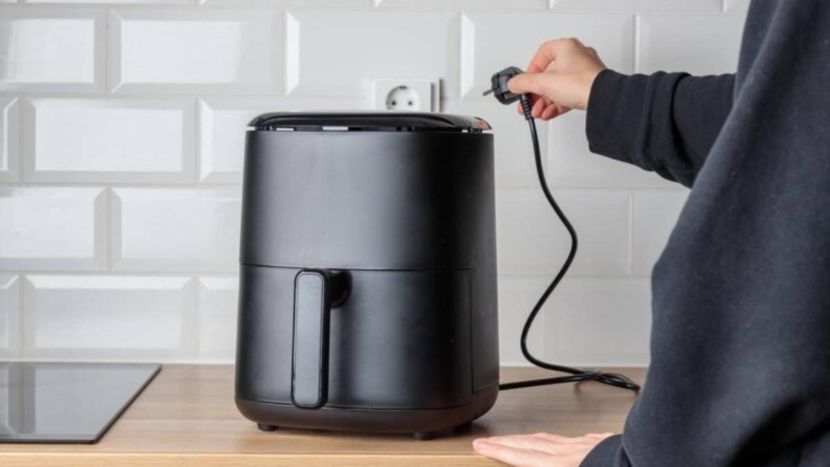 Chica desenchufa la freidora de aire después de haberla utilizado.