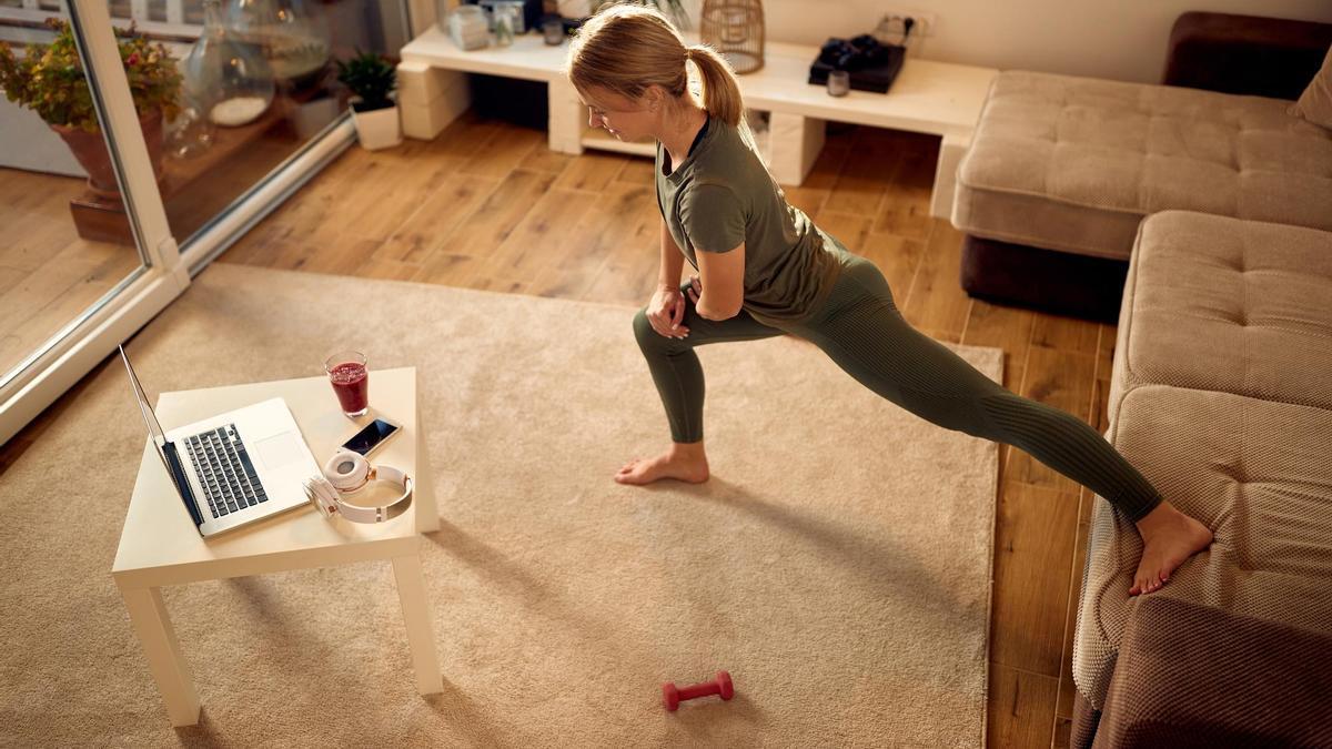 Una mujer realiza un estiramiento en el salón de su casa.
