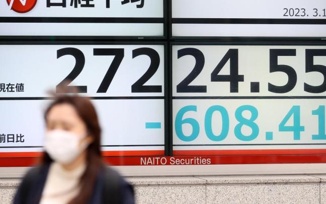 Una mujer pasa por un cartel que refleja la caída bursátil en Japón. Una mujer pasa por un cartel que refleja la caída bursátil en Japón.