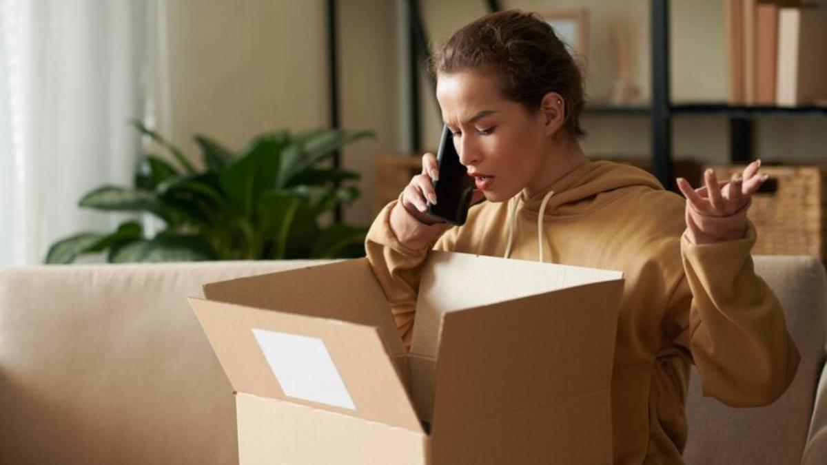 Mujer joven que tiene una conversación por teléfono móvil con el servicio de entrega tras abrir su paquete