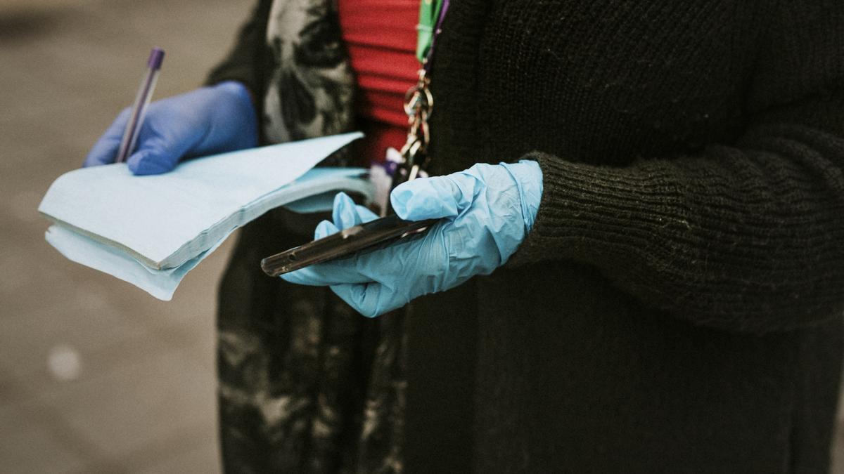 Una mujer con guantes de látex sostiene un teléfono y una libreta.