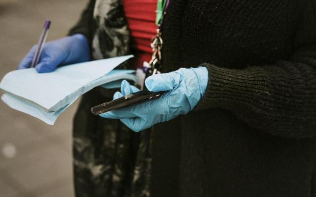 Una mujer con guantes de látex sostiene un teléfono y una libreta.
