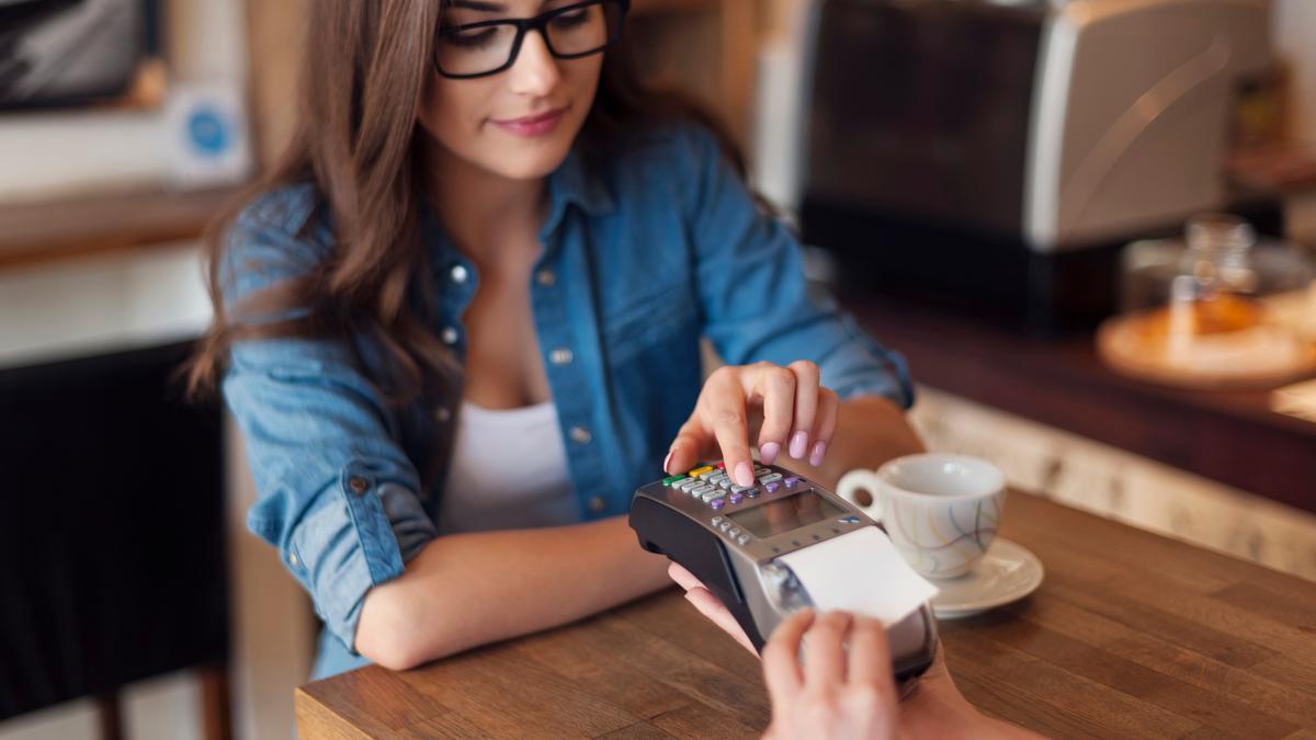 Una joven espera su recibo tras pagar en una cafetería con su tarjeta.