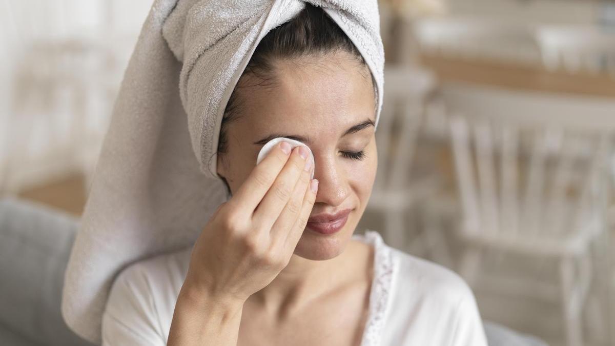Chica se desmaquilla los ojos con ayuda de un algodón.