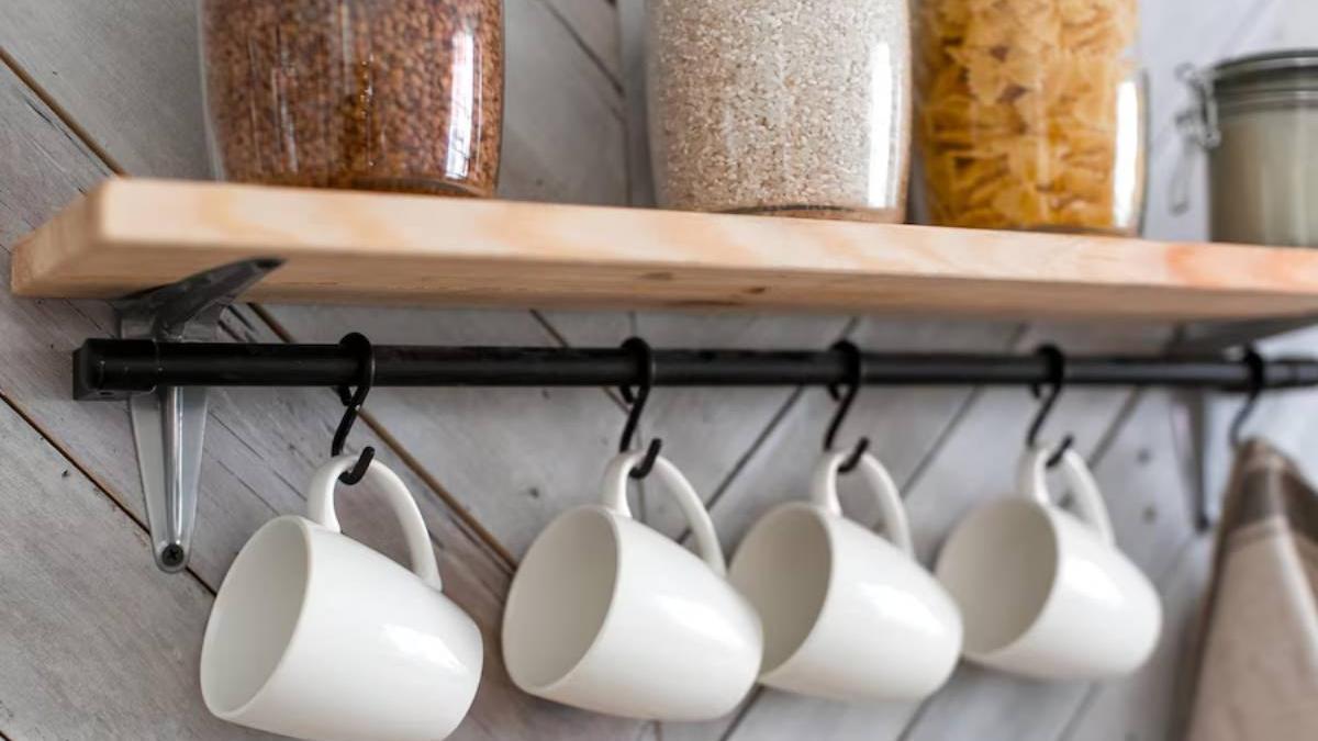 Tazas colgadas en unos ganchos de organización en la cocina debajo de unos botes transparentes para guardar pasta, arroz o cereales