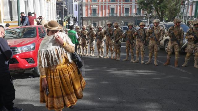 Una mujer se protege del humo frente a unos militares formados frente a la sede del Gobierno de Bolivia