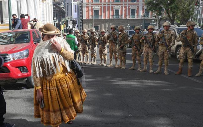 Una mujer se protege del humo frente a unos militares formados frente a la sede del Gobierno de Bolivia / Luis Gandarillas Una mujer se protege del humo frente a unos militares formados frente a la sede del Gobierno de Bolivia