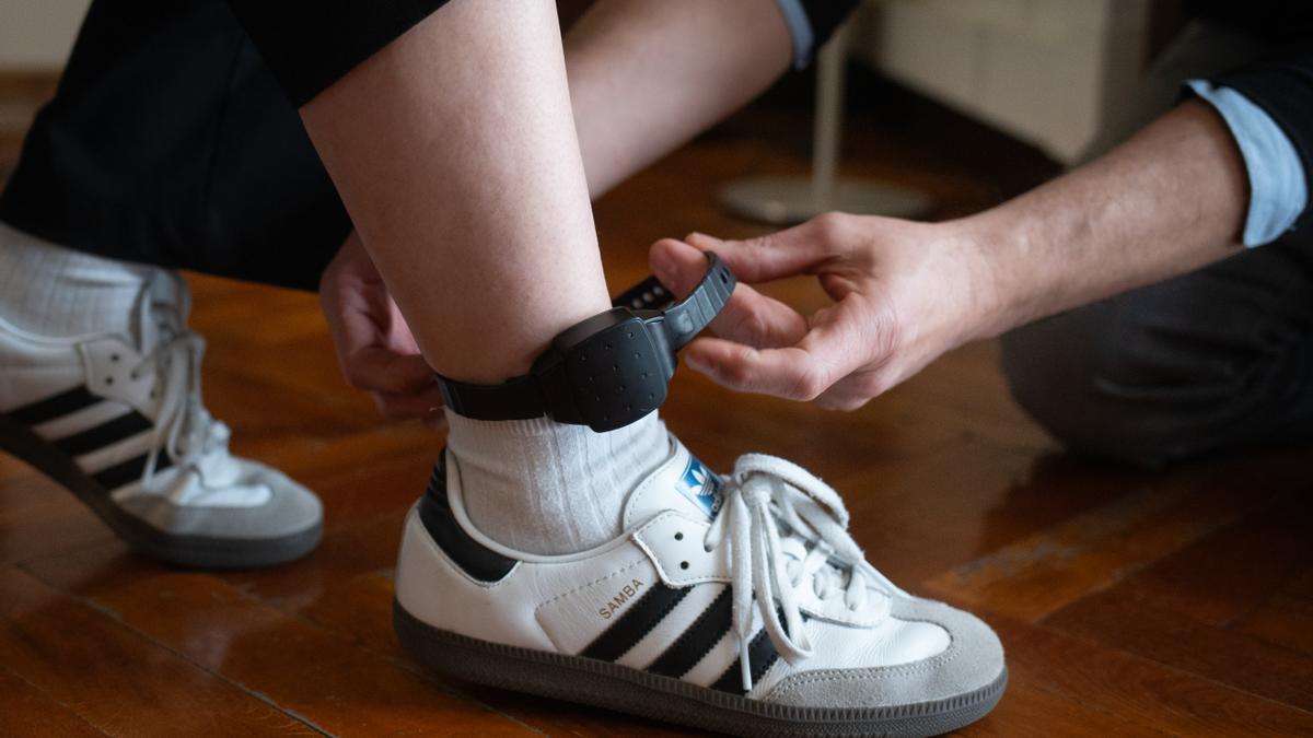 Una persona coloca a otra una pulsera electrónica de geolocalización.