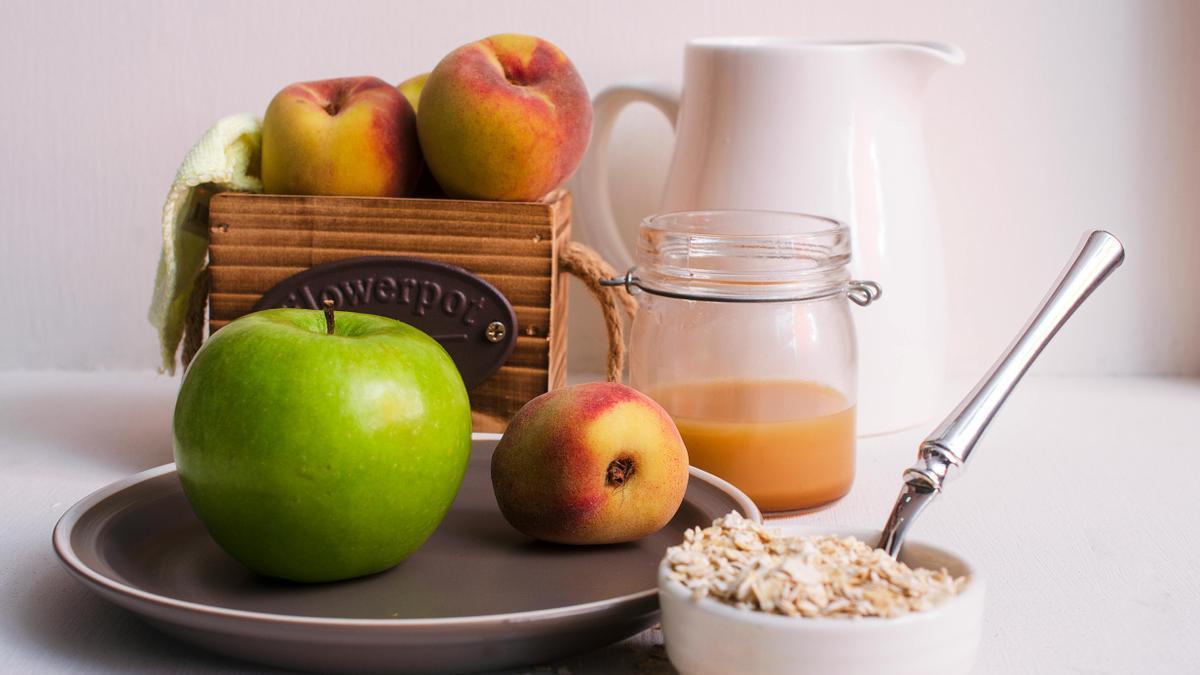 Manzana verde y melocotones junto a un zumo de naranja y avena para el desayuno