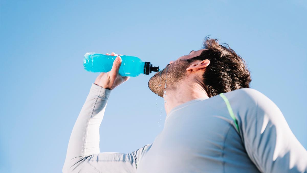 Un hombre bebe una bebida isotónica mientras practica deporte.