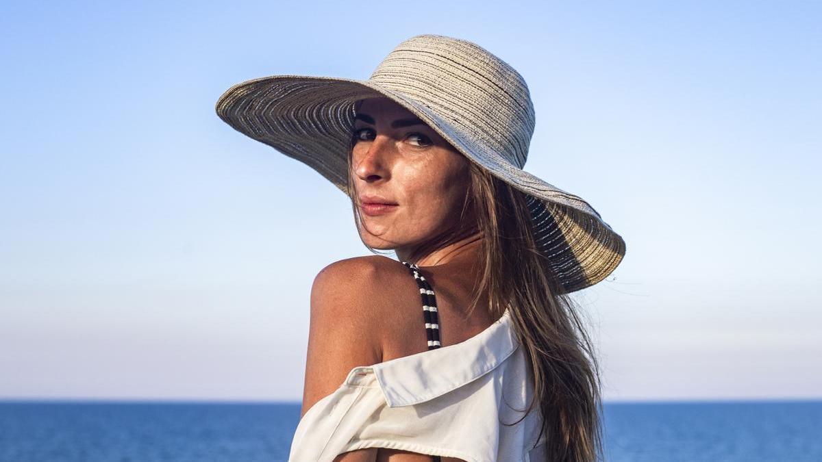 Mujer en la playa con un sombrero para protegerse del sol.