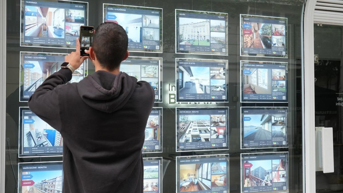 Un joven fotografía las ofertas en el escaparate de una inmobiliaria de Bilbao.