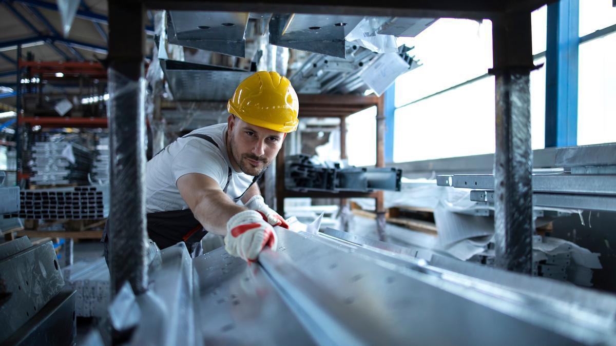 Un trabajador manipula material metálico en una fábrica.