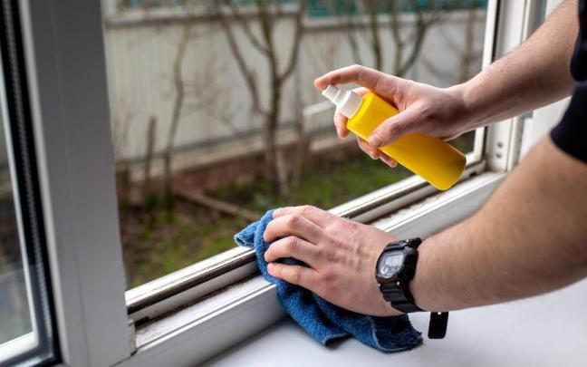 Una persona limpia con una bayeta y un spray el riel de una ventana.