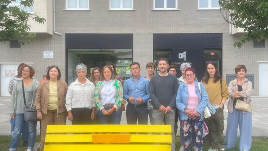 Banco pintado de amarillo en Otamotzena, con representantes del Ayuntamiento y vecinos al fondo.