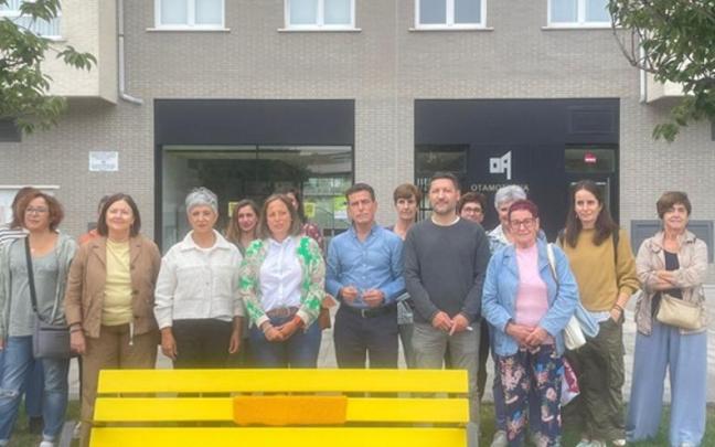 Banco pintado de amarillo en Otamotzena, con representantes del Ayuntamiento y vecinos al fondo.