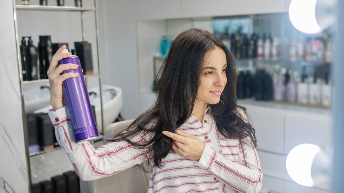 Una mujer se rocía laca para mantener el peinado.