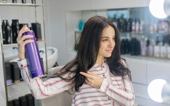 Una mujer se rocía laca para mantener el peinado.