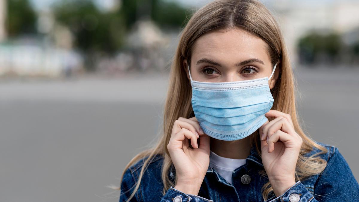 Una mujer cubre su boca con una mascarilla quirúrgica.