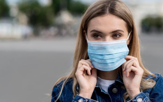 Una mujer cubre su boca con una mascarilla quirúrgica.