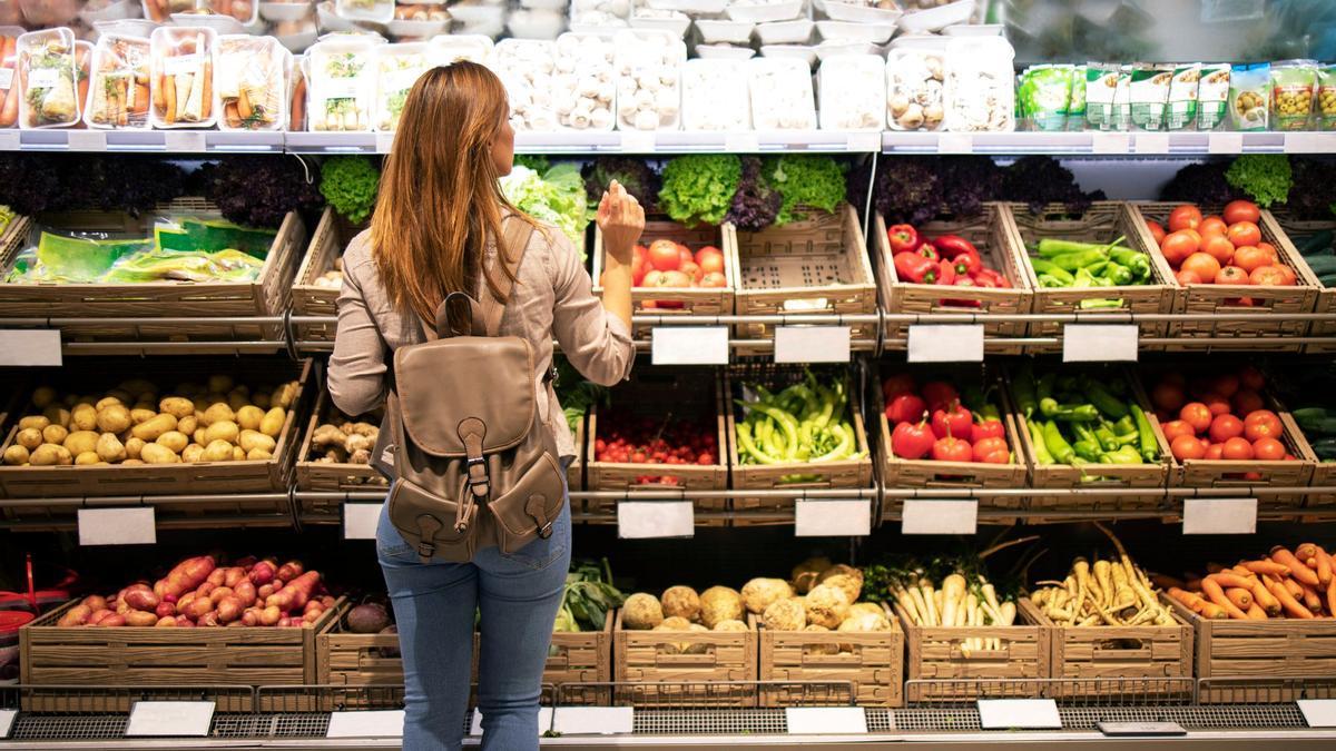 Una mujer elige entre varias verduras en un supermercado.
